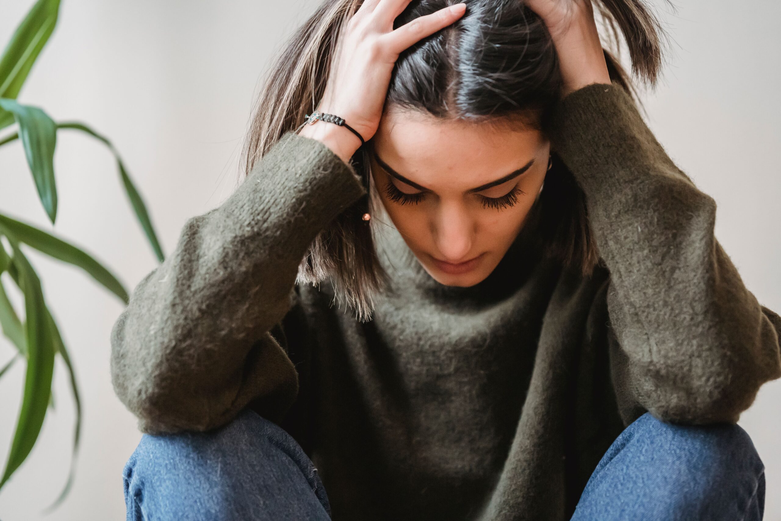girl sitting on floor with elbows on knees holding her hair expressing the stress of figuring out what are the physical symptoms of anxiety